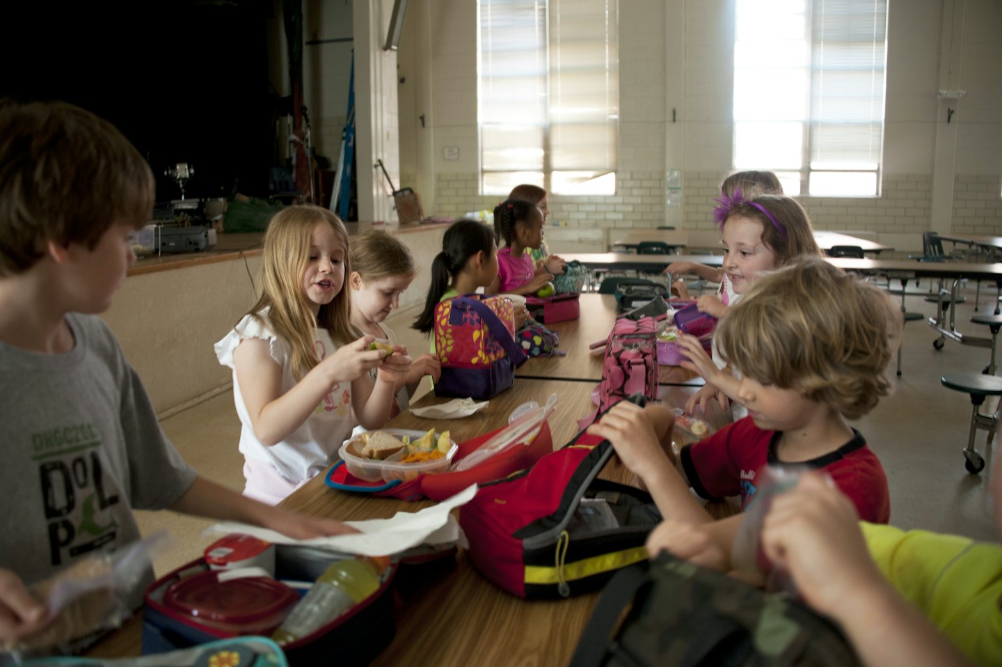 Children eating lunch together at tables in a school hall.