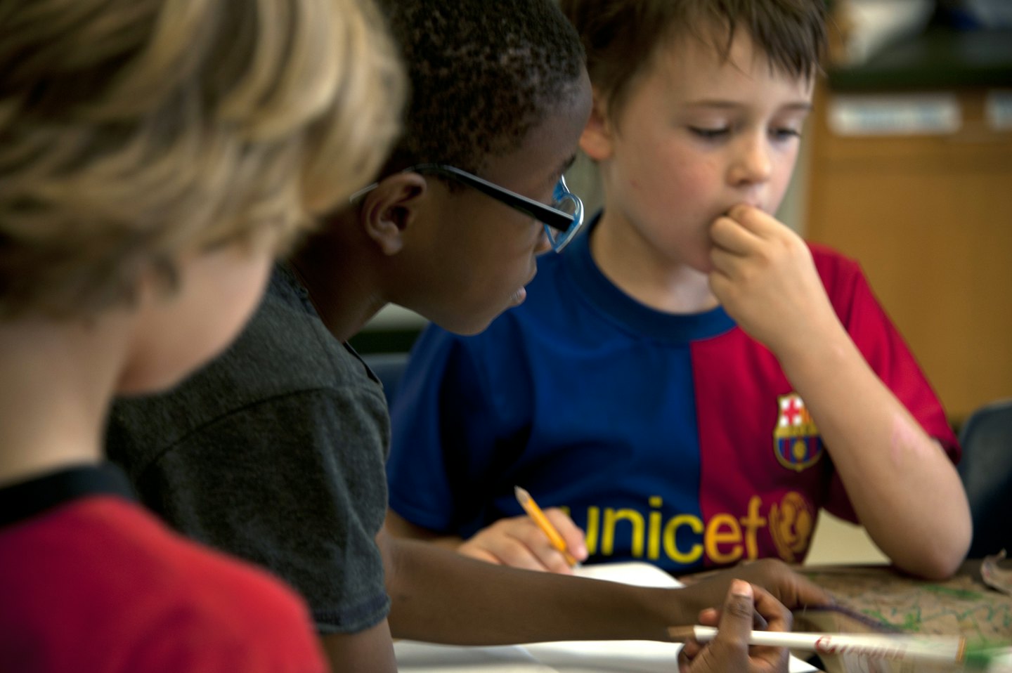 Three young children working together at a table with pencils.