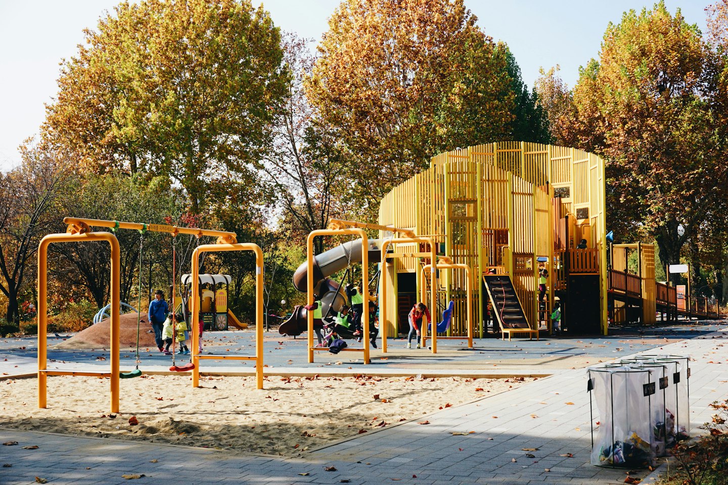 Children play on a wooden playground structure with yellow swings in autumn.