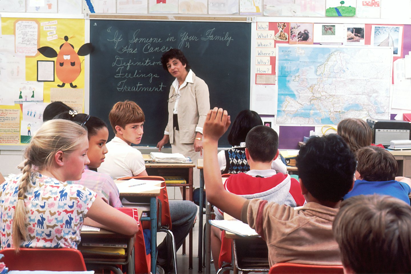 Teacher at the front of the classroom with students at their desks.