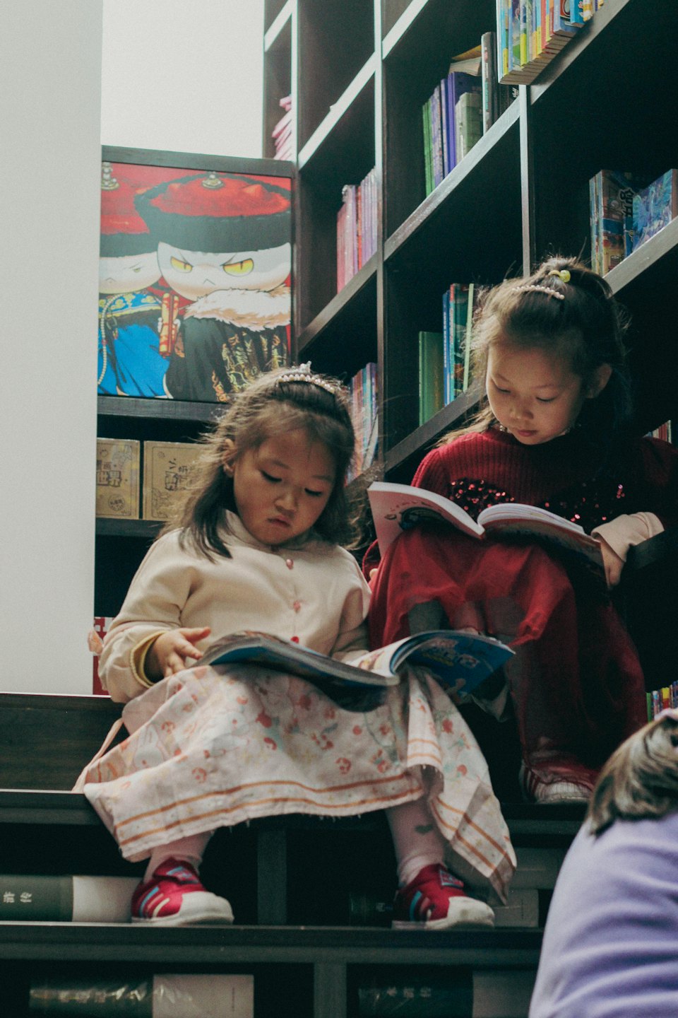 Two girls sitting on library steps reading their books.